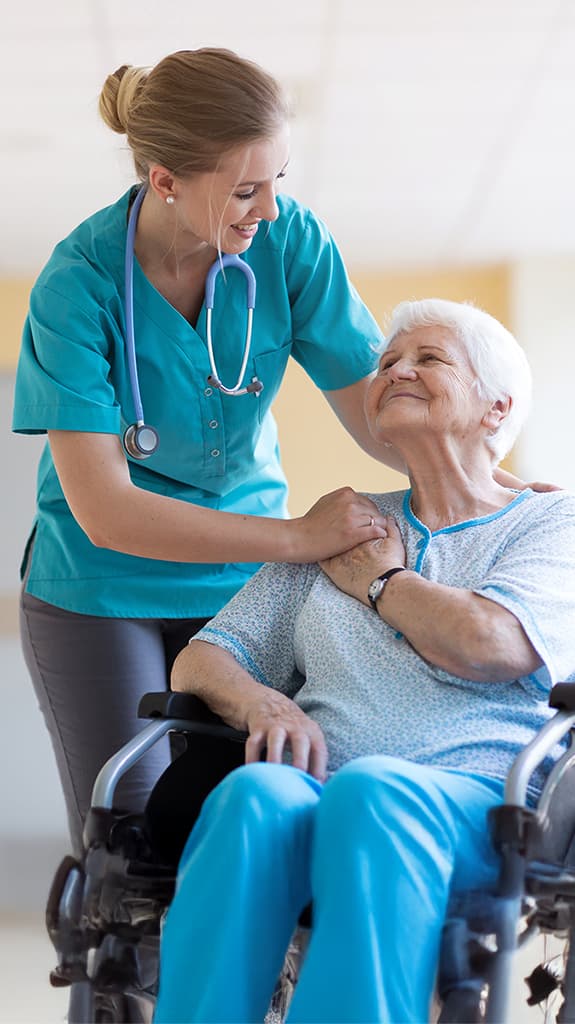 Eine Ärztin legt fürsorglich die Arme auf eine Patientin die im Rollstuhl sitzt.