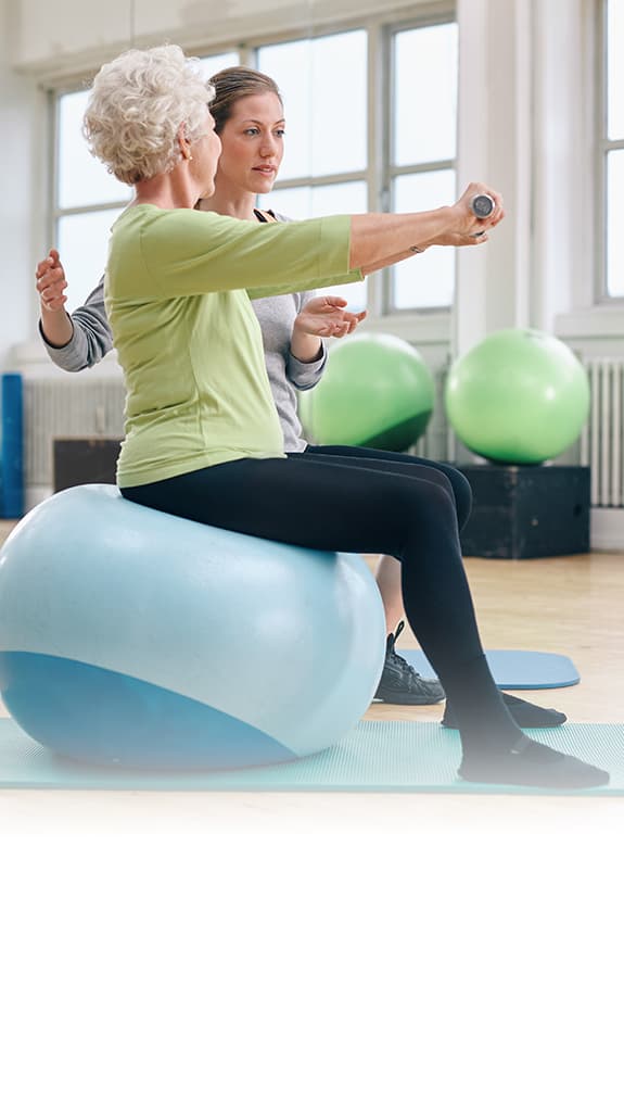 Eine Physiotherapeutin macht Übungen mit einer älteren Frau auf einem Sitzball.