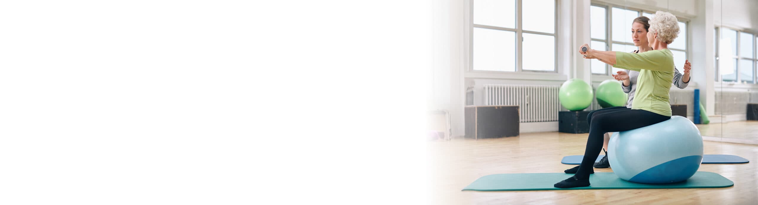 Eine Physiotherapeutin macht Übungen mit einer älteren Frau auf einem Sitzball.