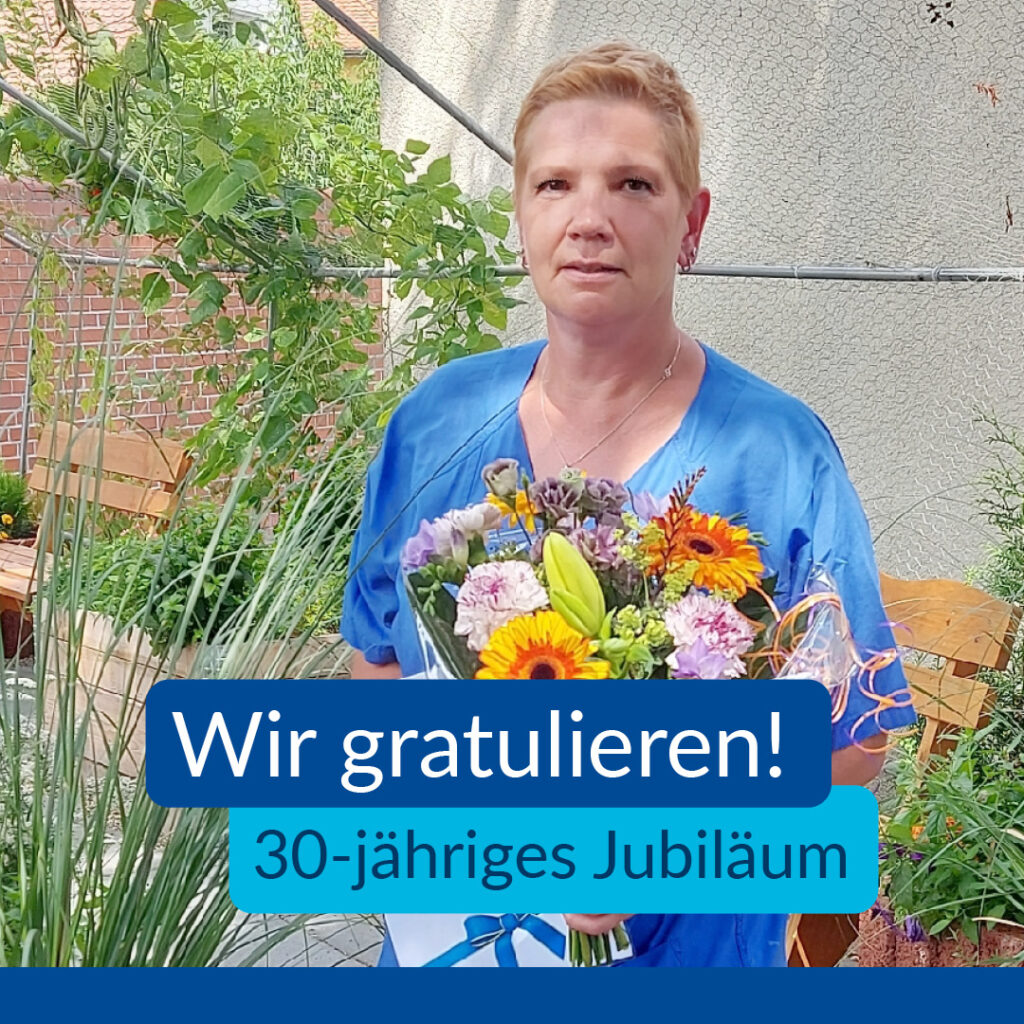 Auf dem Bild sieht man Uta Beutler, welche in unserem Kräutergarten steht und Blumen in der Hand hält. Im Text, gratulieren wir ihr zum 30-jährigem Jubiläum.