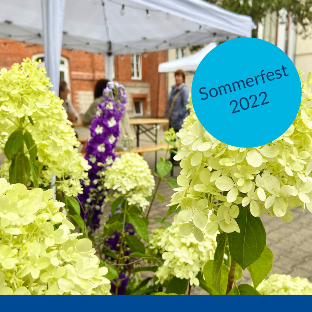 Im Vordergrund des Bildes sieht man Blumen, dahinter Sitzbänke unter einem Schirm. Im Text steht: "Sommerfest 2022".
