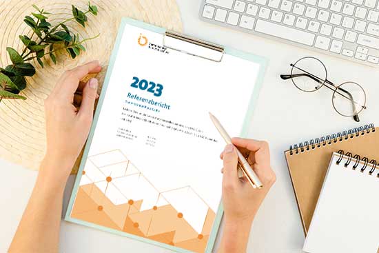 Aufsicht auf einen Schreibtisch. Sichtbar sind zwei Hände und ein Klemmbrett mit einem Qualitätsbersicht 2023
